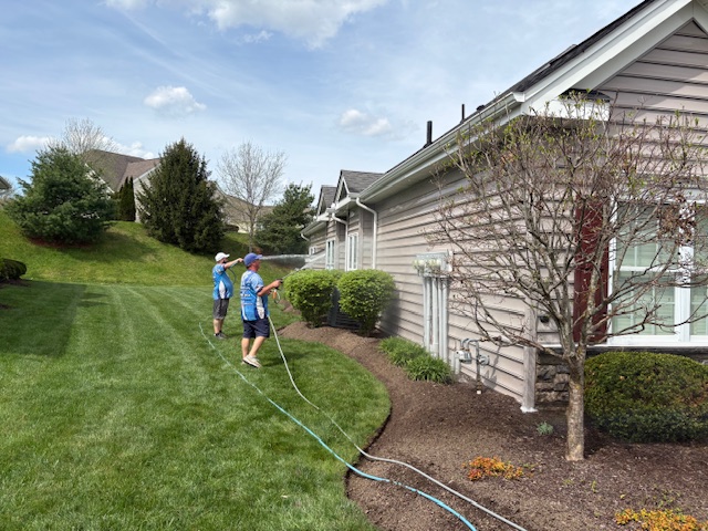 Two team members using pressure-washing equipment beside a house