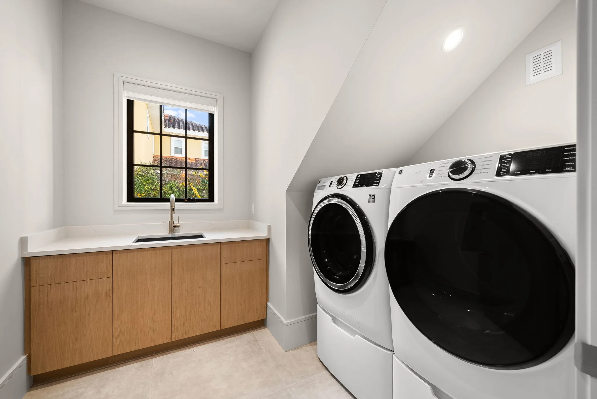 A laundry room with white front-loading machines, a wooden countertop and a sink.