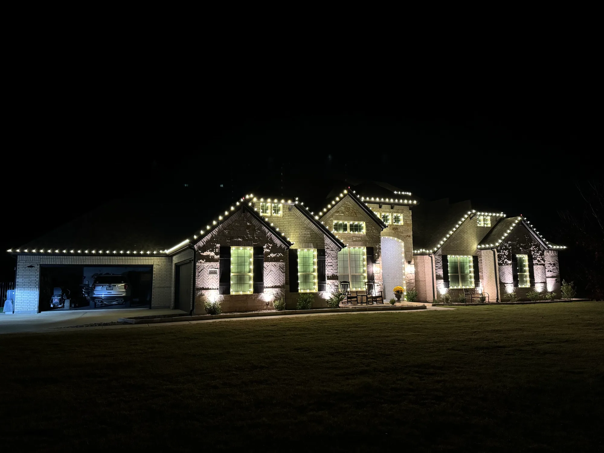 Wide single-storey brick home lit at night in warm white, with the full roofline traced and every front window outlined.