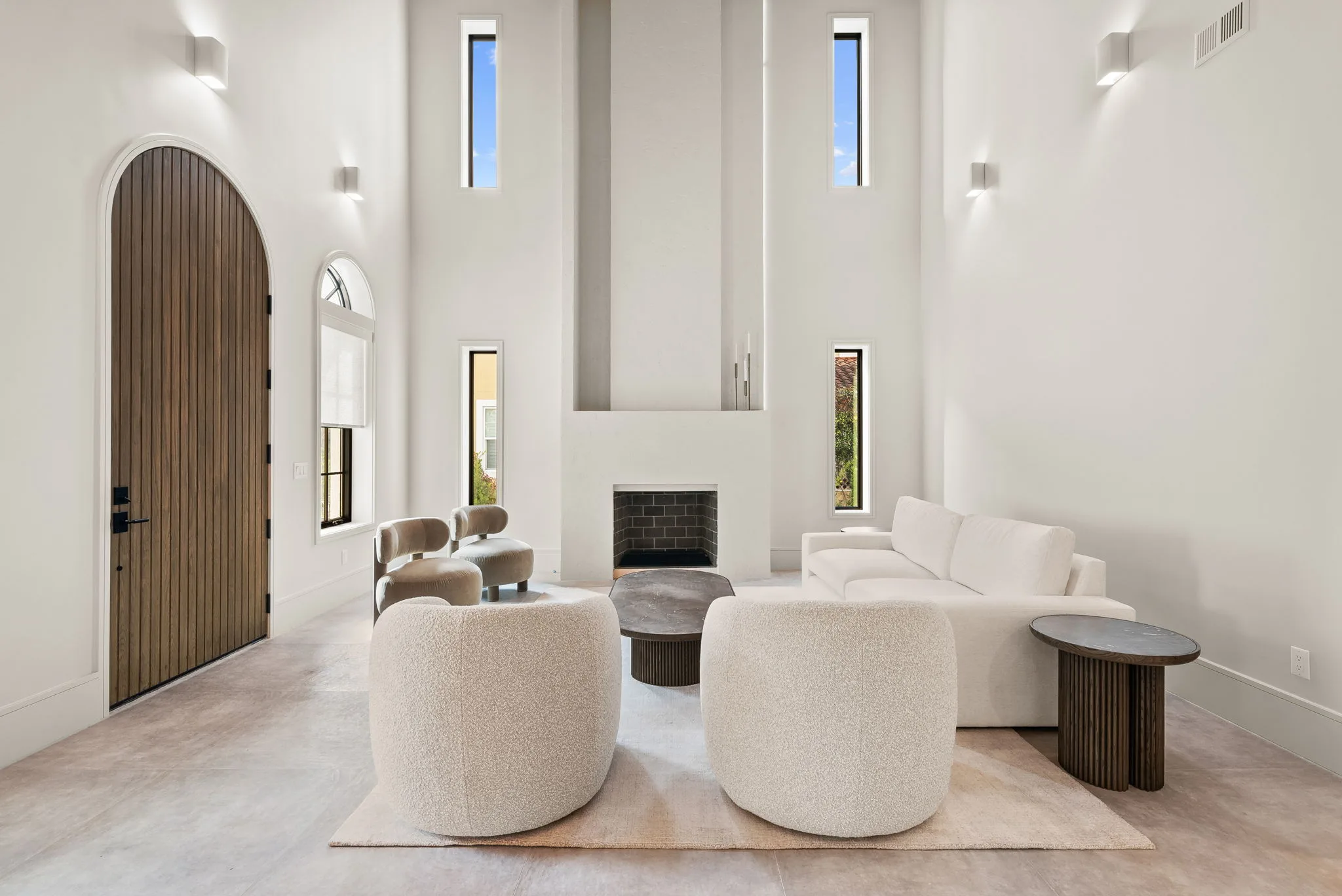 A bright living room with a sofa, round chairs, a minimalist fireplace and tall windows.