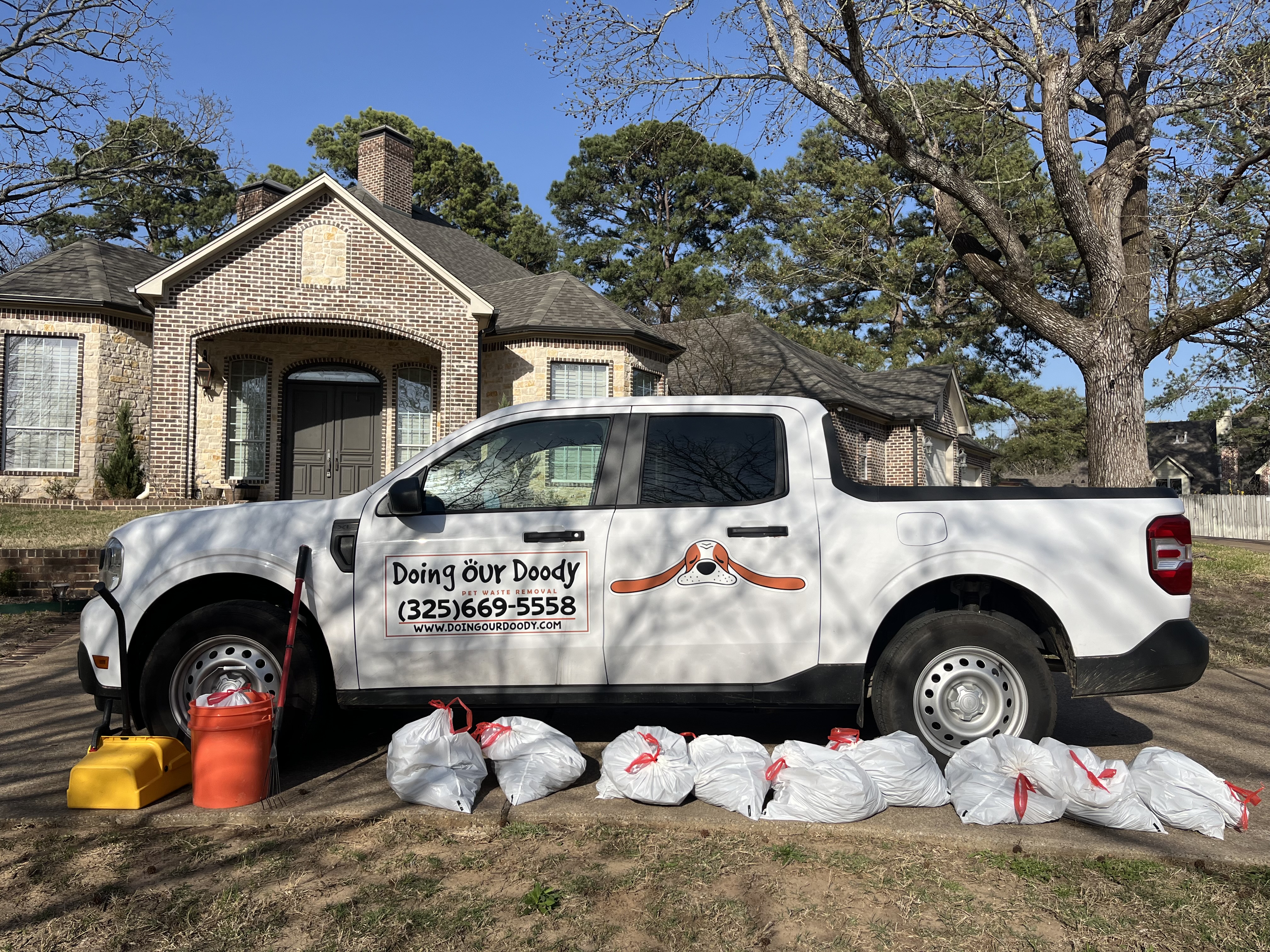 Doing Our Doody white pickup truck parked in front of a brick house with collected waste bags