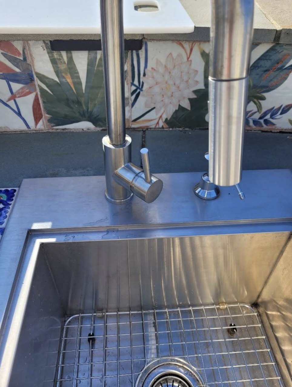 Modern stainless steel kitchen sink with single-handle faucet against decorative floral tile