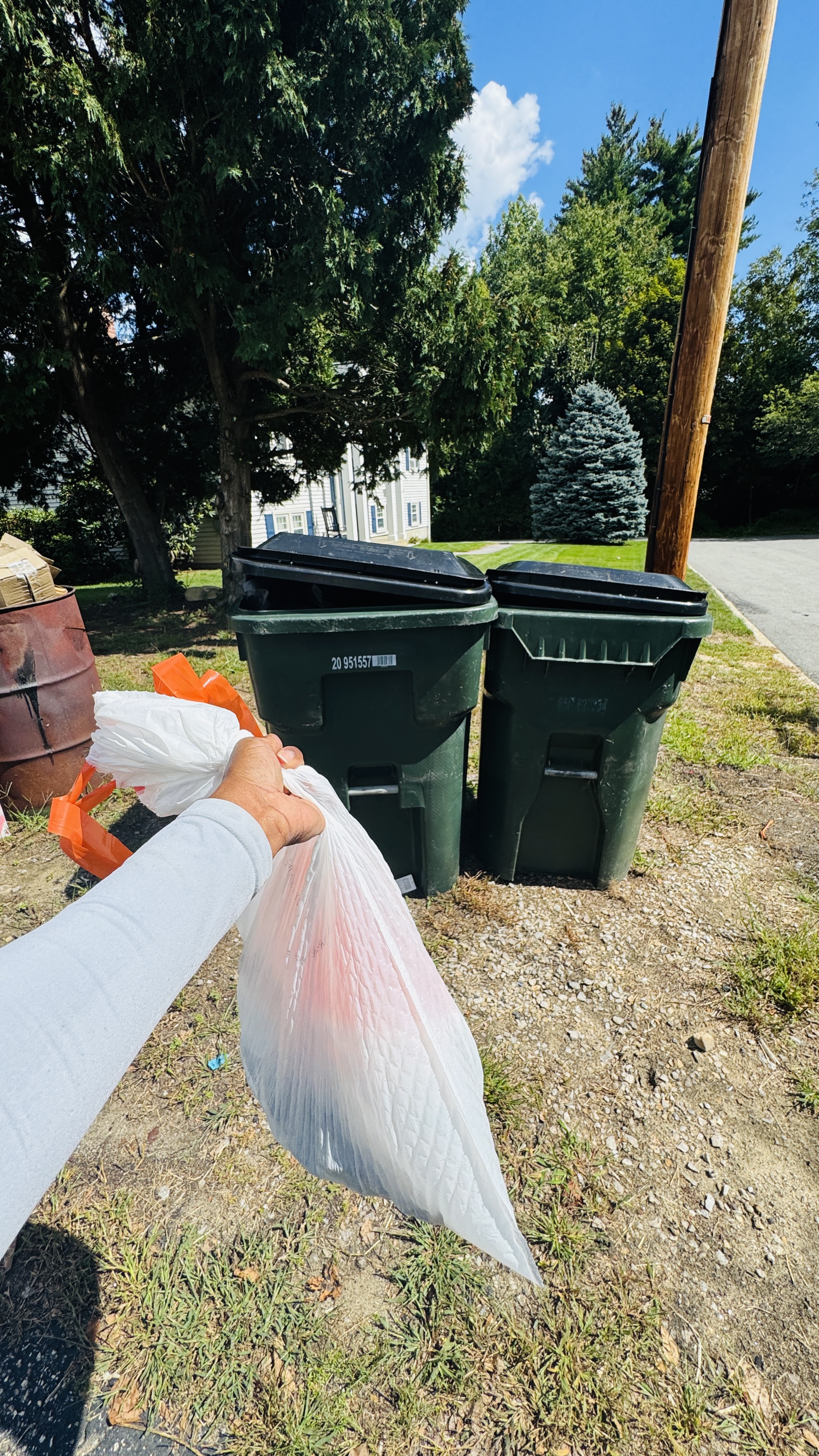 Technician carrying a tied bag of pet waste to a pair of green outdoor trash barrels