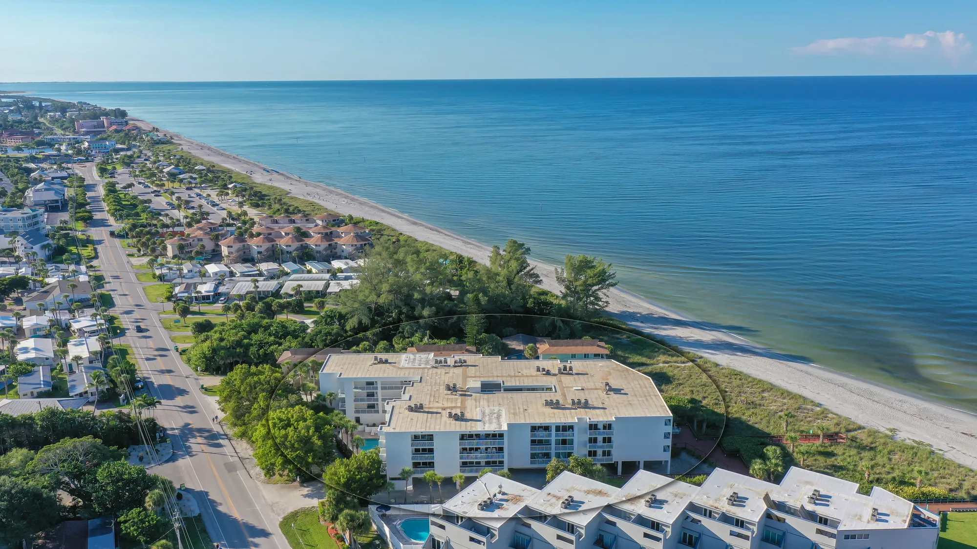 Aerial of The Surf Club, a low-rise beachfront building, with the Gulf of Mexico stretching out beyond it.