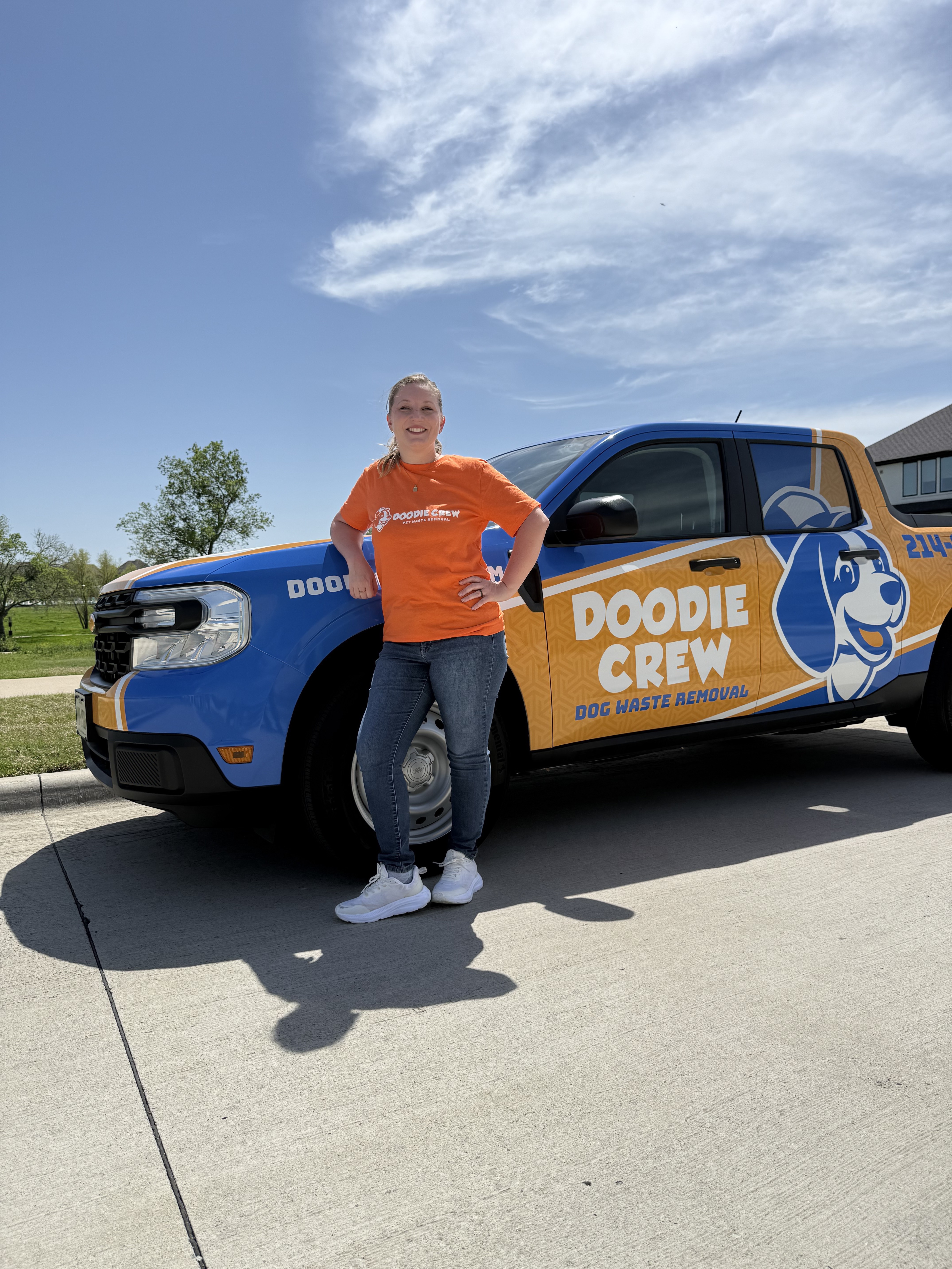 A smiling Doodie Crew employee standing in front of the branded truck