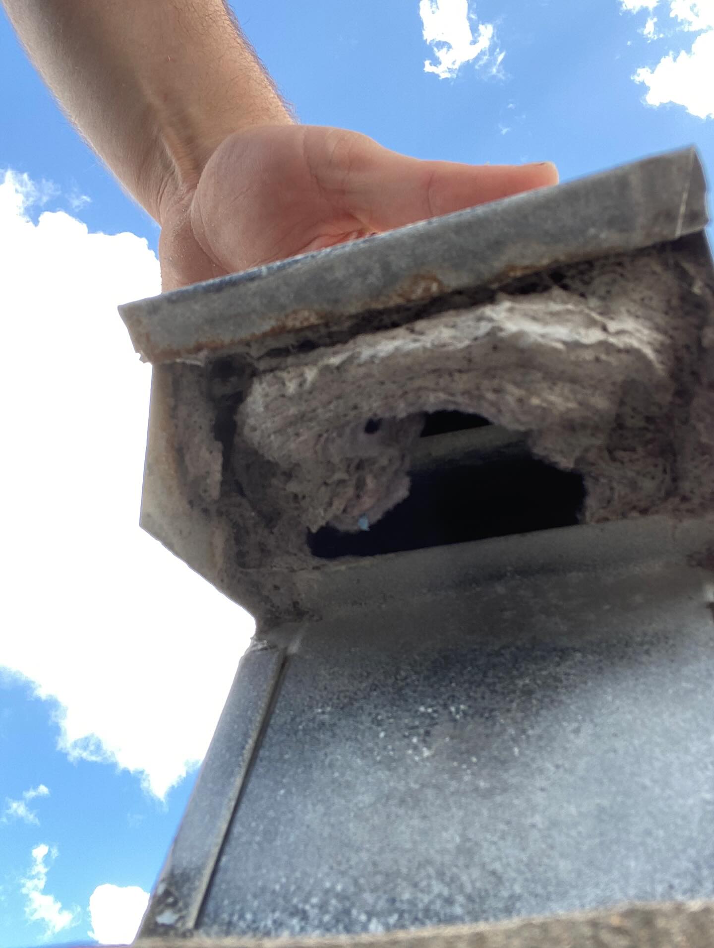 A hand holding a damaged chimney flue with visible cracks against a blue sky