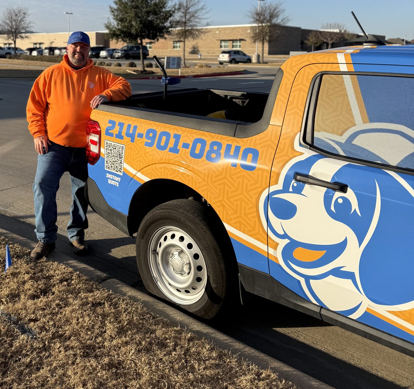 Man in an orange hoodie standing next to a blue and orange Doodie Crew branded delivery truck featuring a cartoon dog logo, contact number, and QR code for an instant quote