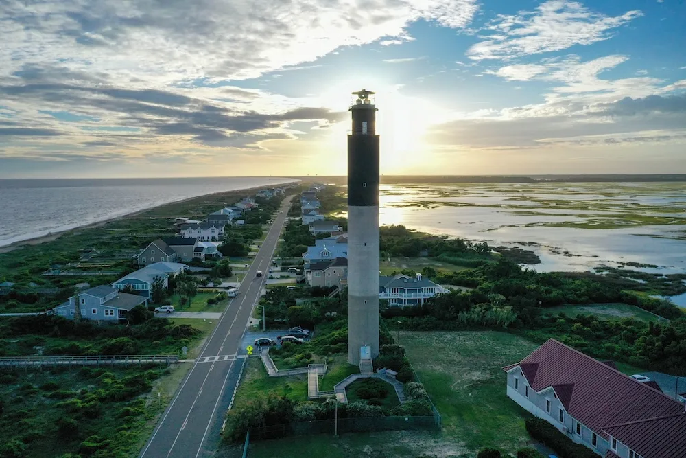 Oak Island NC coastal lighthouse at sunset with residential and marsh areas