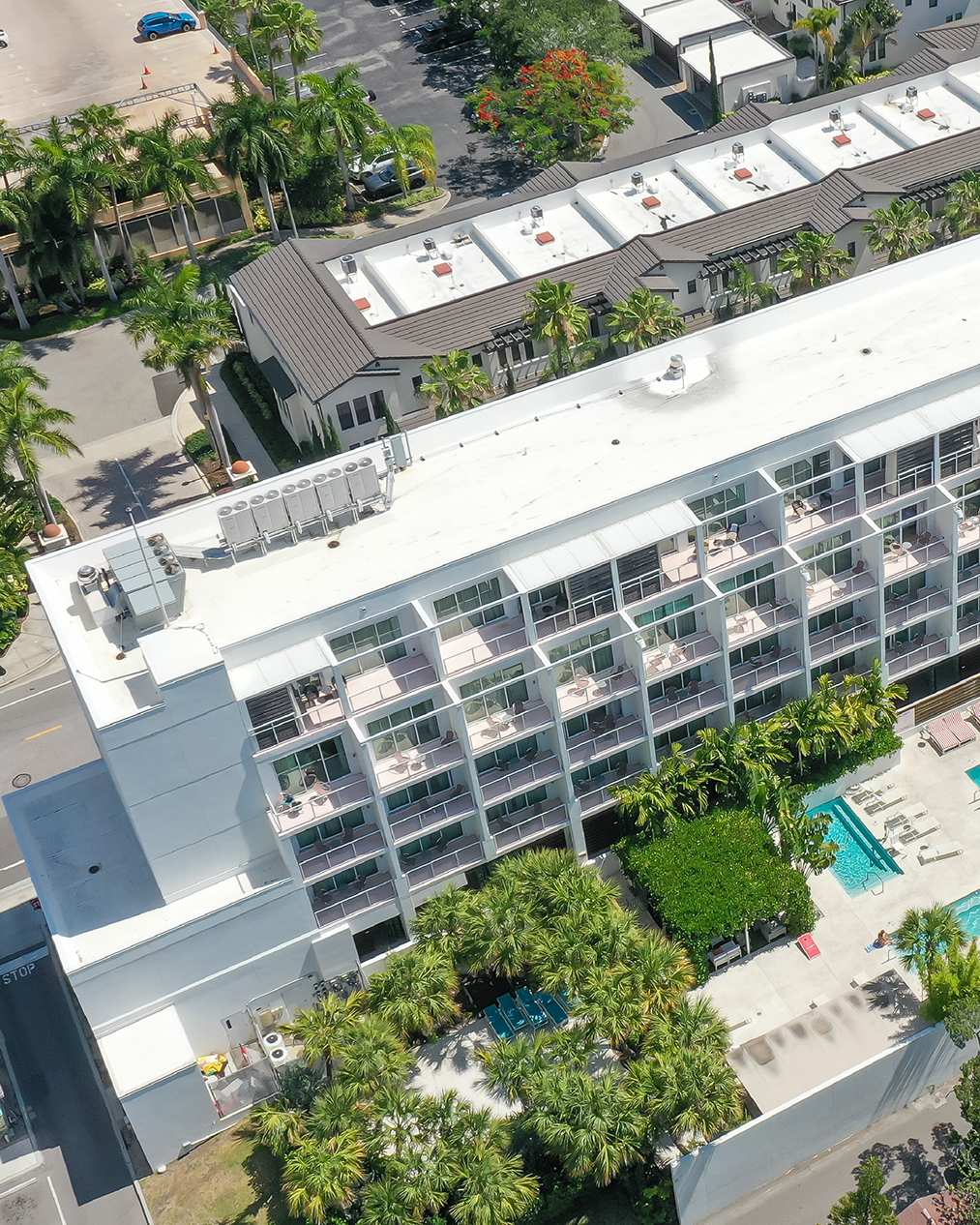 Aerial of The Collection Residences in Sarasota, a white multi-storey residential building among the downtown low-rise blocks, with the Gulf beyond.