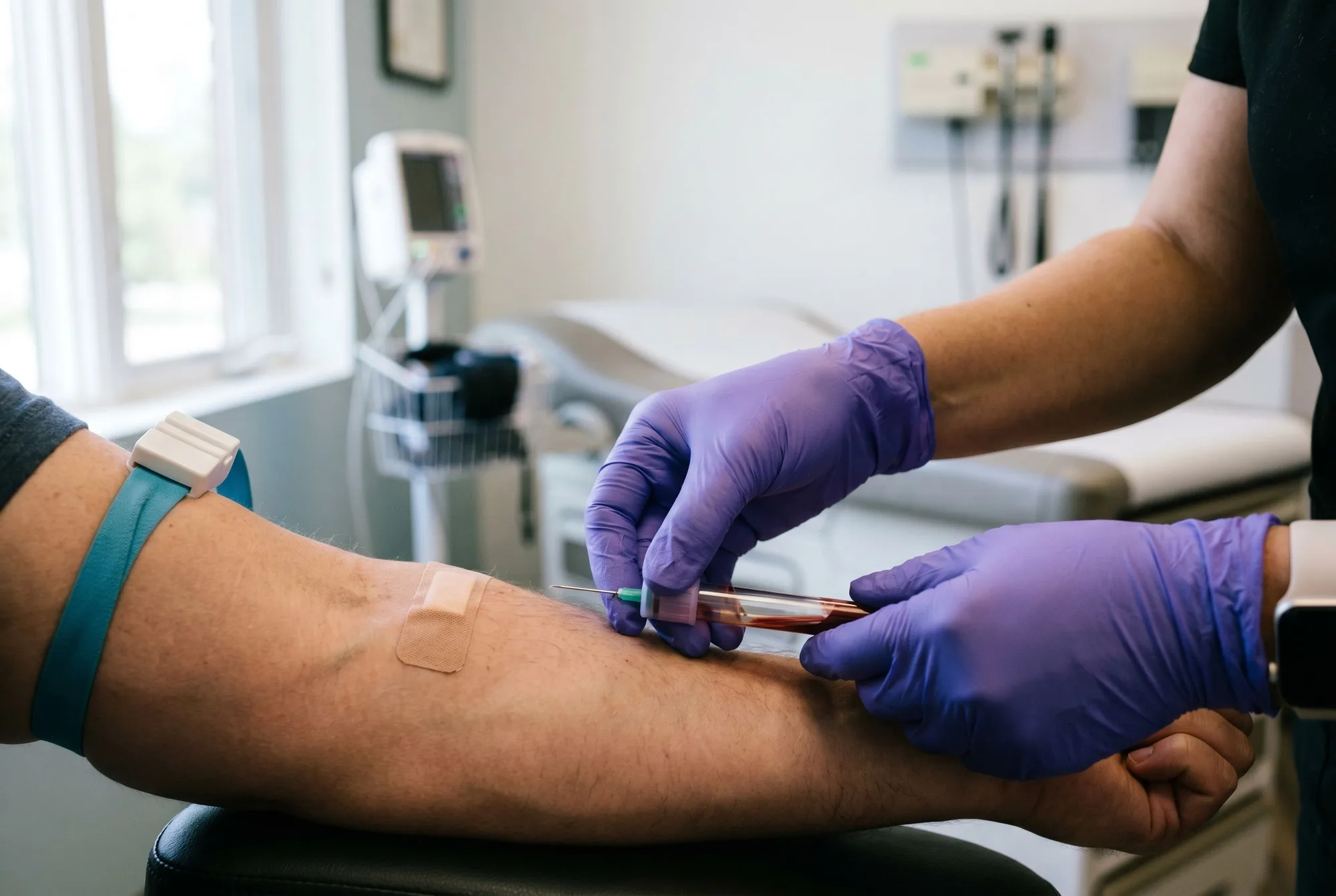 A clinician in gloves performing a therapeutic blood draw in an exam room at Forge Health & Performance.
