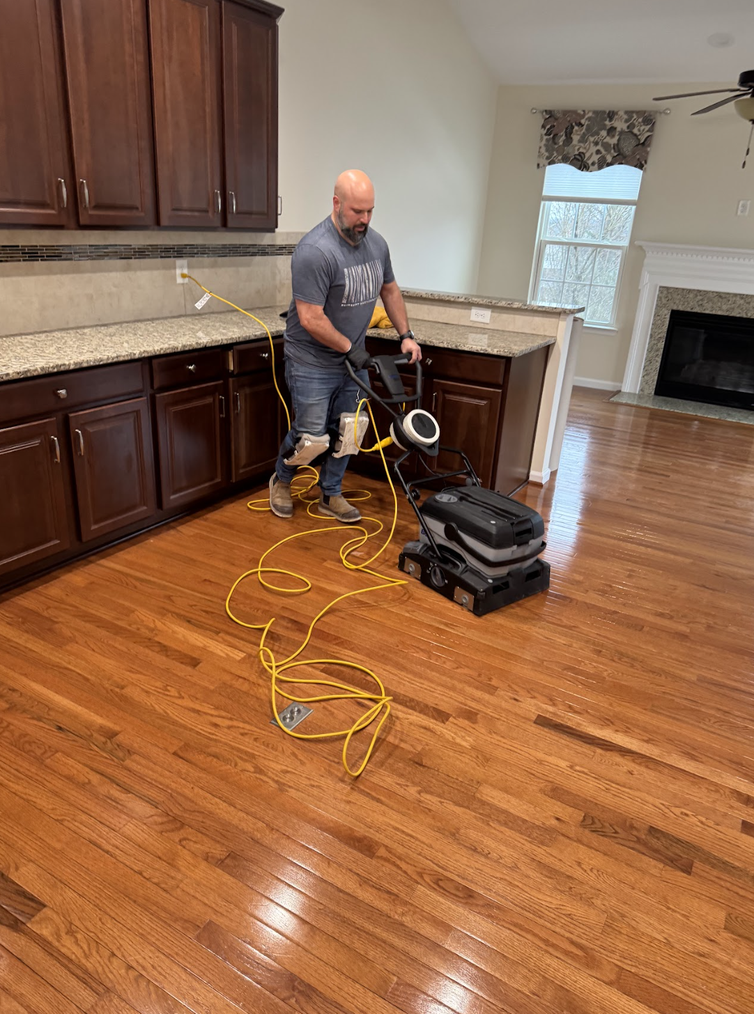 Technician using floor buffing machine on polished hardwood floor in kitchen