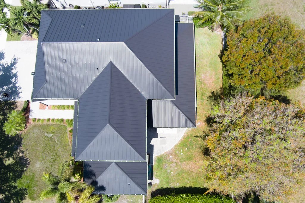 Aerial view of a modern home with a sleek dark metal roof surrounded by tropical greenery