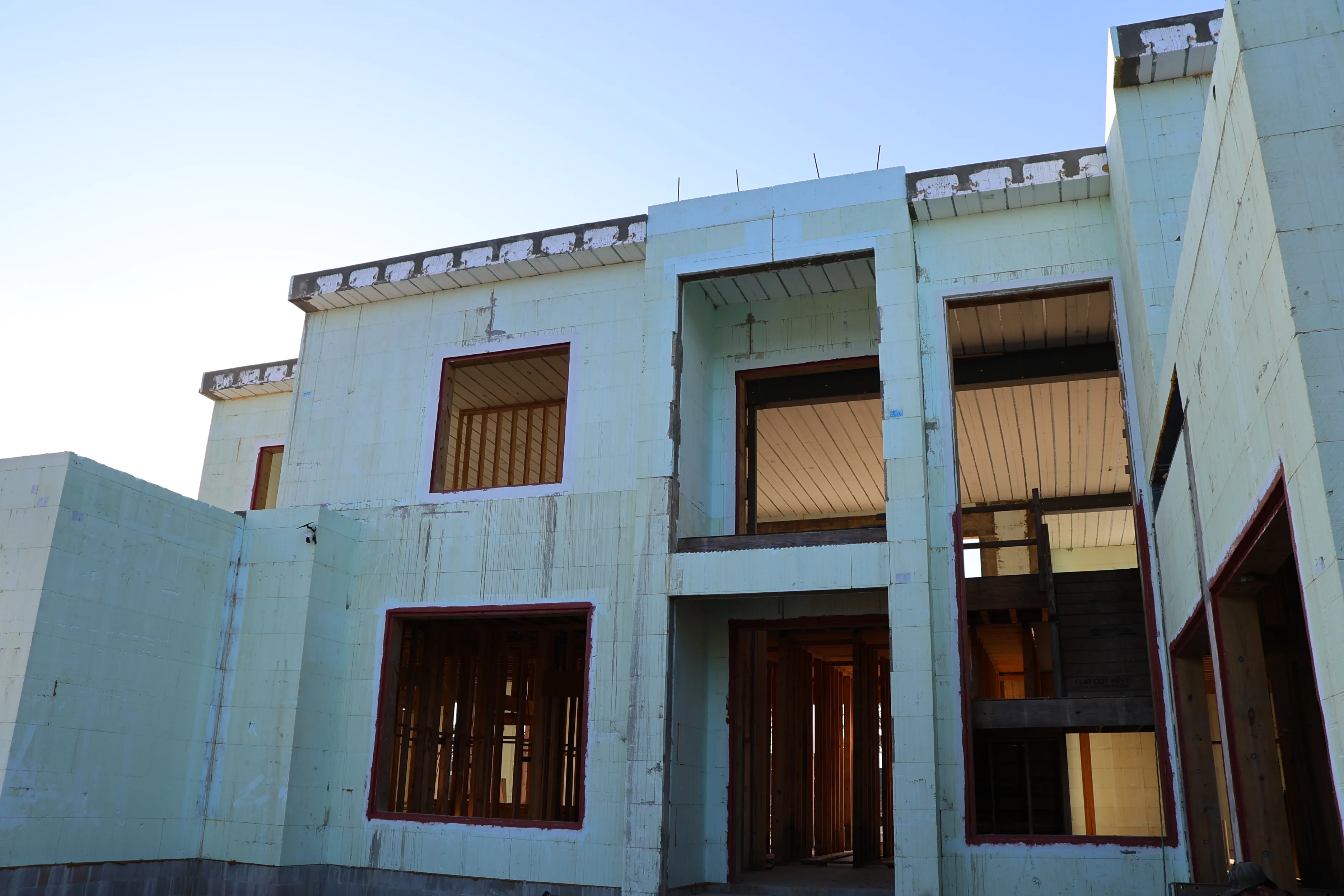 A three-storey concrete shell under construction by JAT Specialties, with formed walls and openings cut for tall windows.