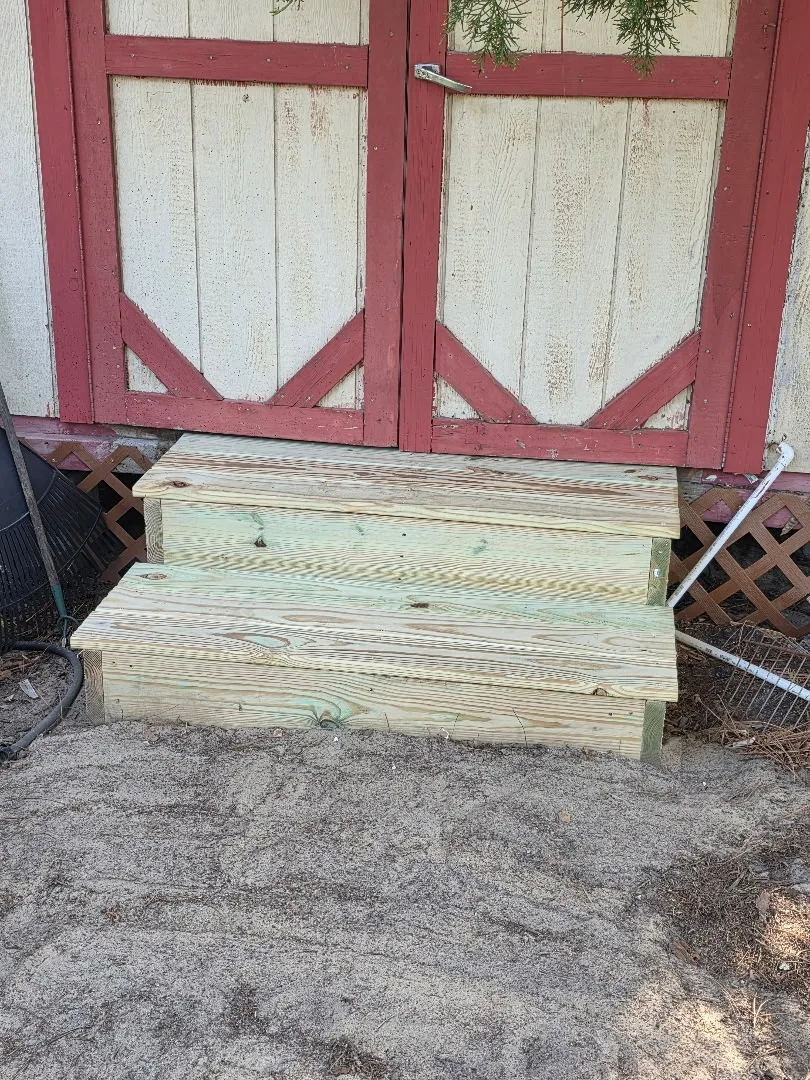 Wooden steps leading to a red-framed double door — exterior carpentry work in progress