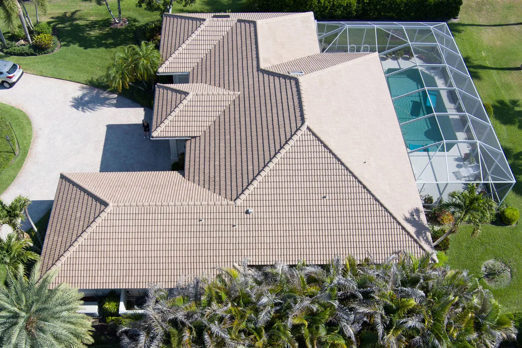 Aerial drone view of a single-story Florida home with clay tile roof, screened pool and tropical landscaping