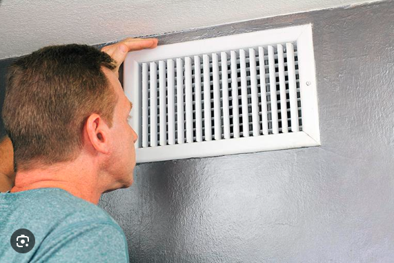 A man closely inspecting a wall-mounted air vent