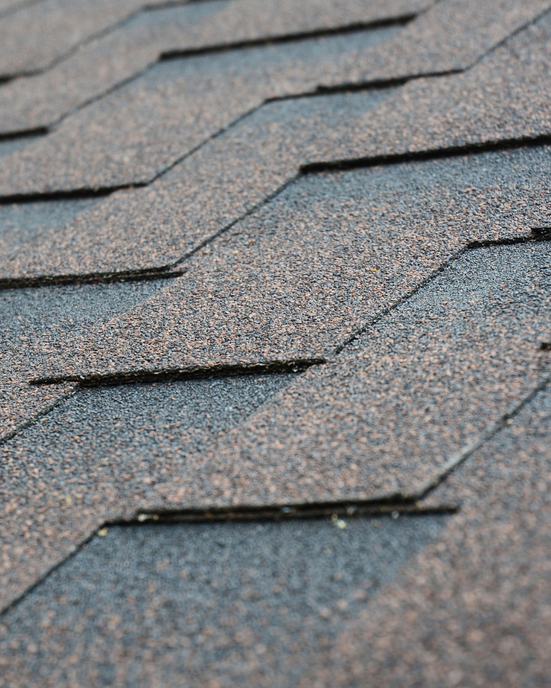 Close-up view of asphalt shingles on a roof with a textured, layered pattern in shades of gray and brown