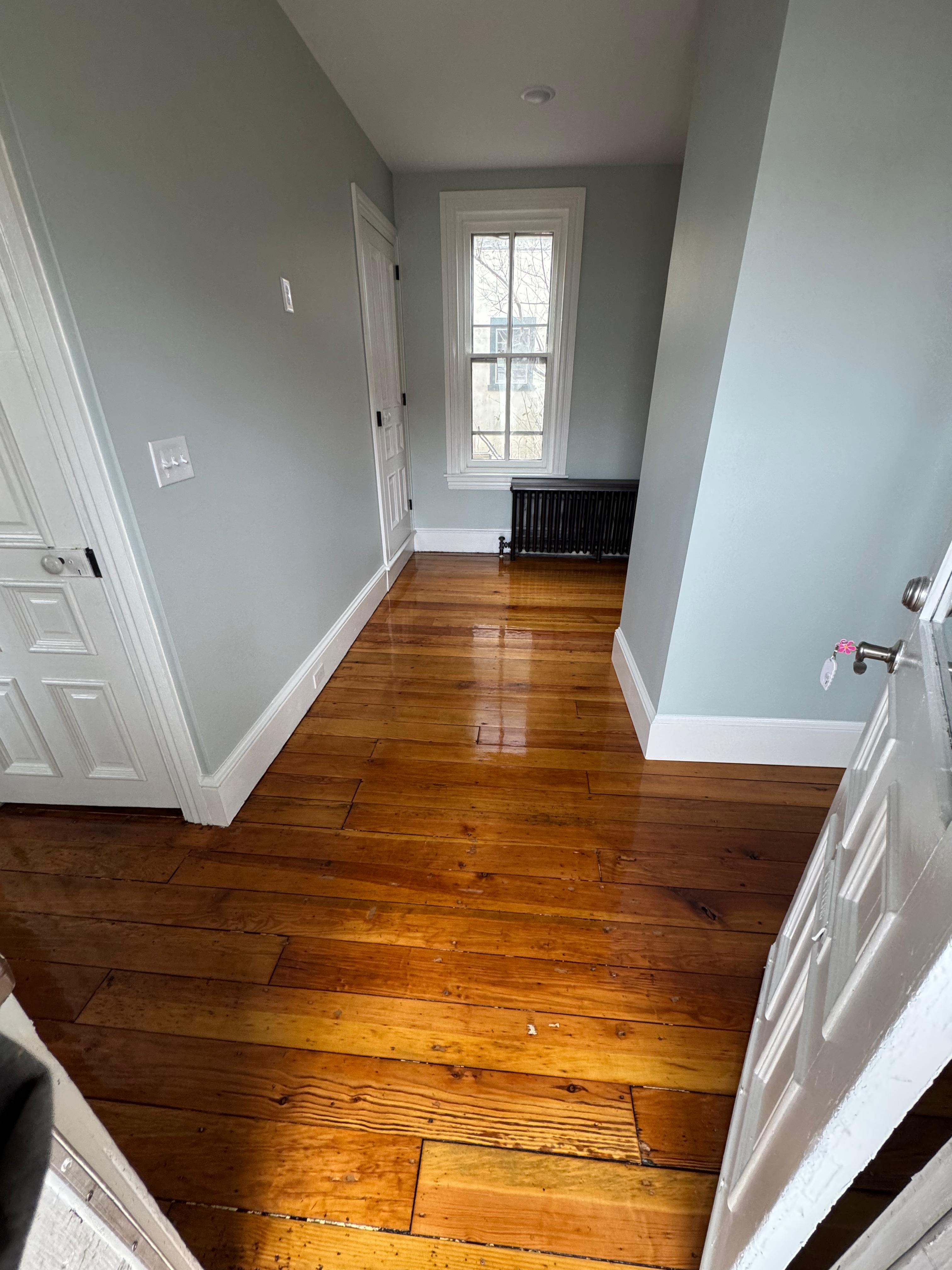 Well-lit hallway with polished wooden floors and light gray walls