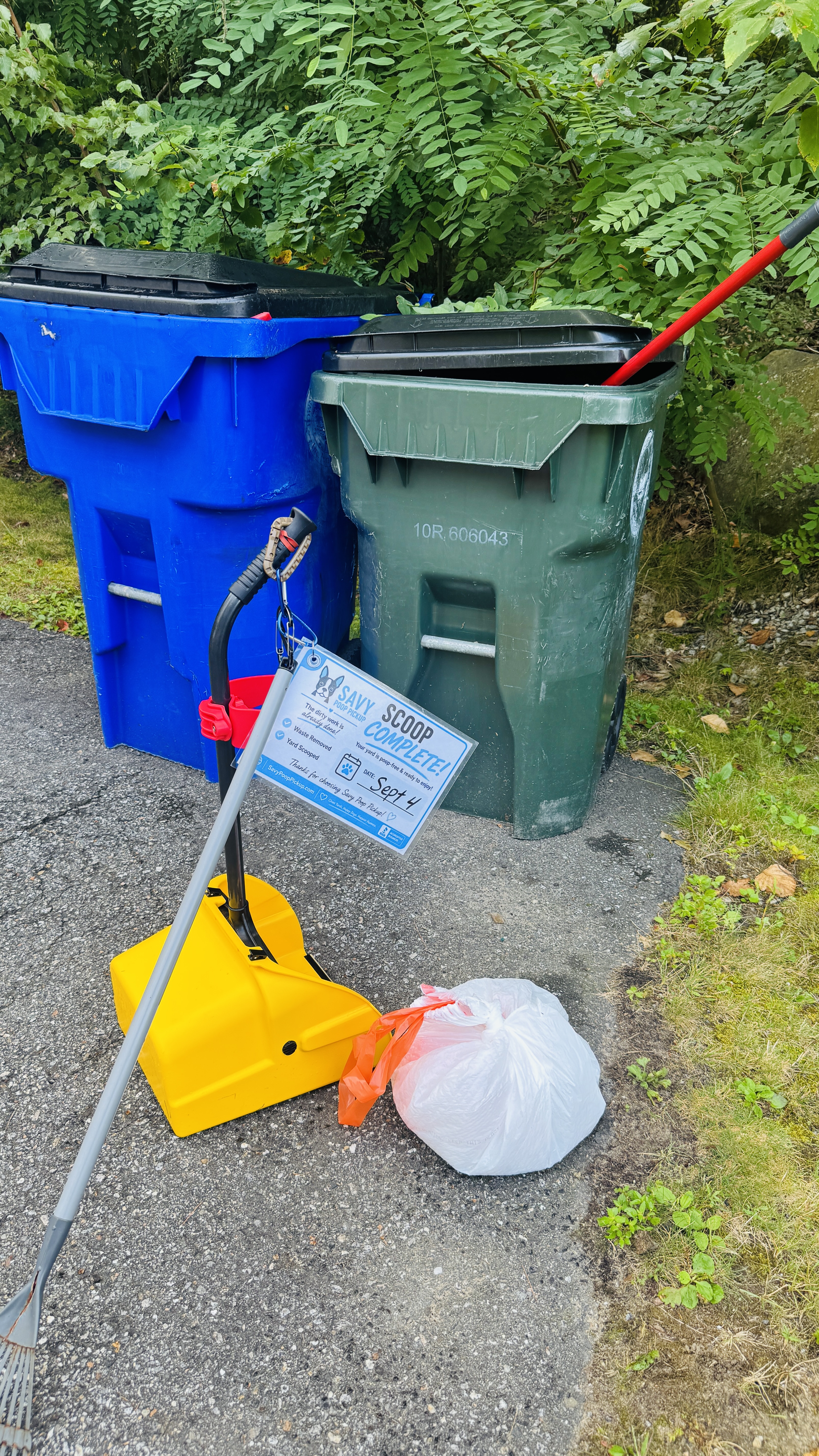 Yellow pet waste scooper and a bagged pickup beside blue and green barrels with a service completion tag