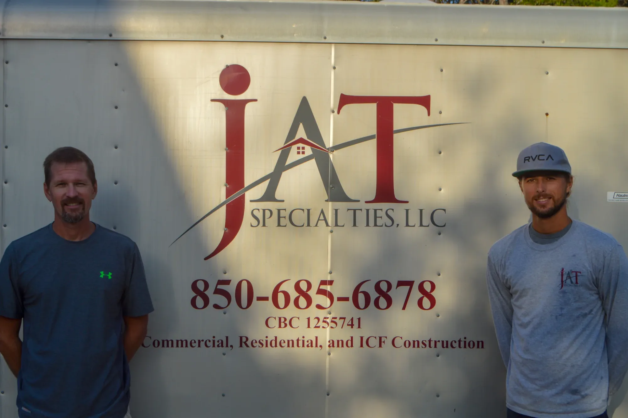 Jeremy and Mitchell Trantina standing either side of the lettered JAT Specialties company trailer.