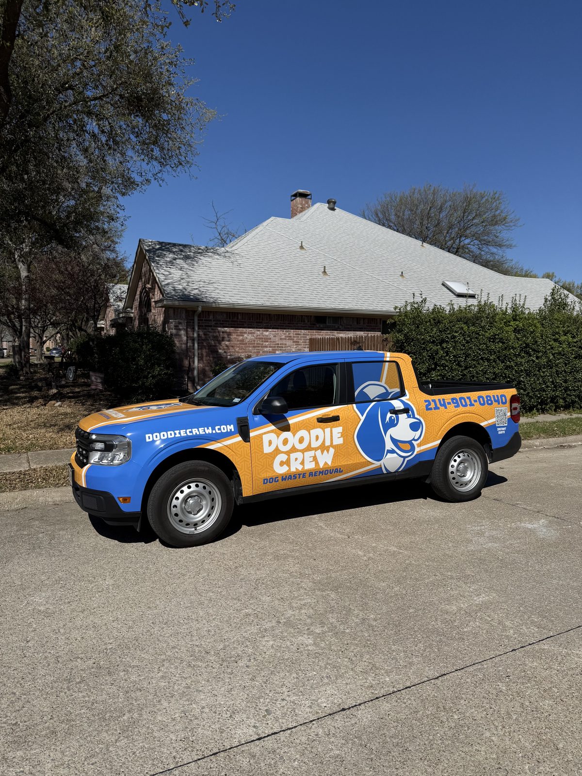 Doodie Crew branded pickup truck parked on a residential street in Prosper, TX with house and clear blue sky in the background