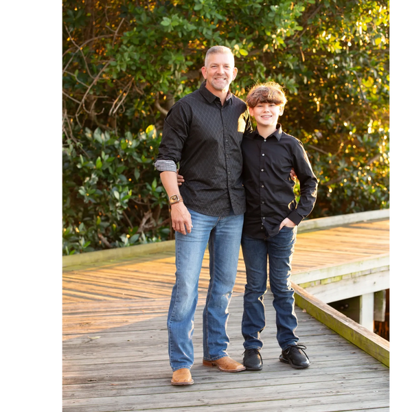 A man and his son standing together on a wooden dock, smiling at the camera