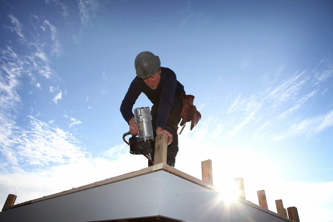 A helmeted roofing professional using tools at a roof edge during a maintenance job on the Treasure Coast