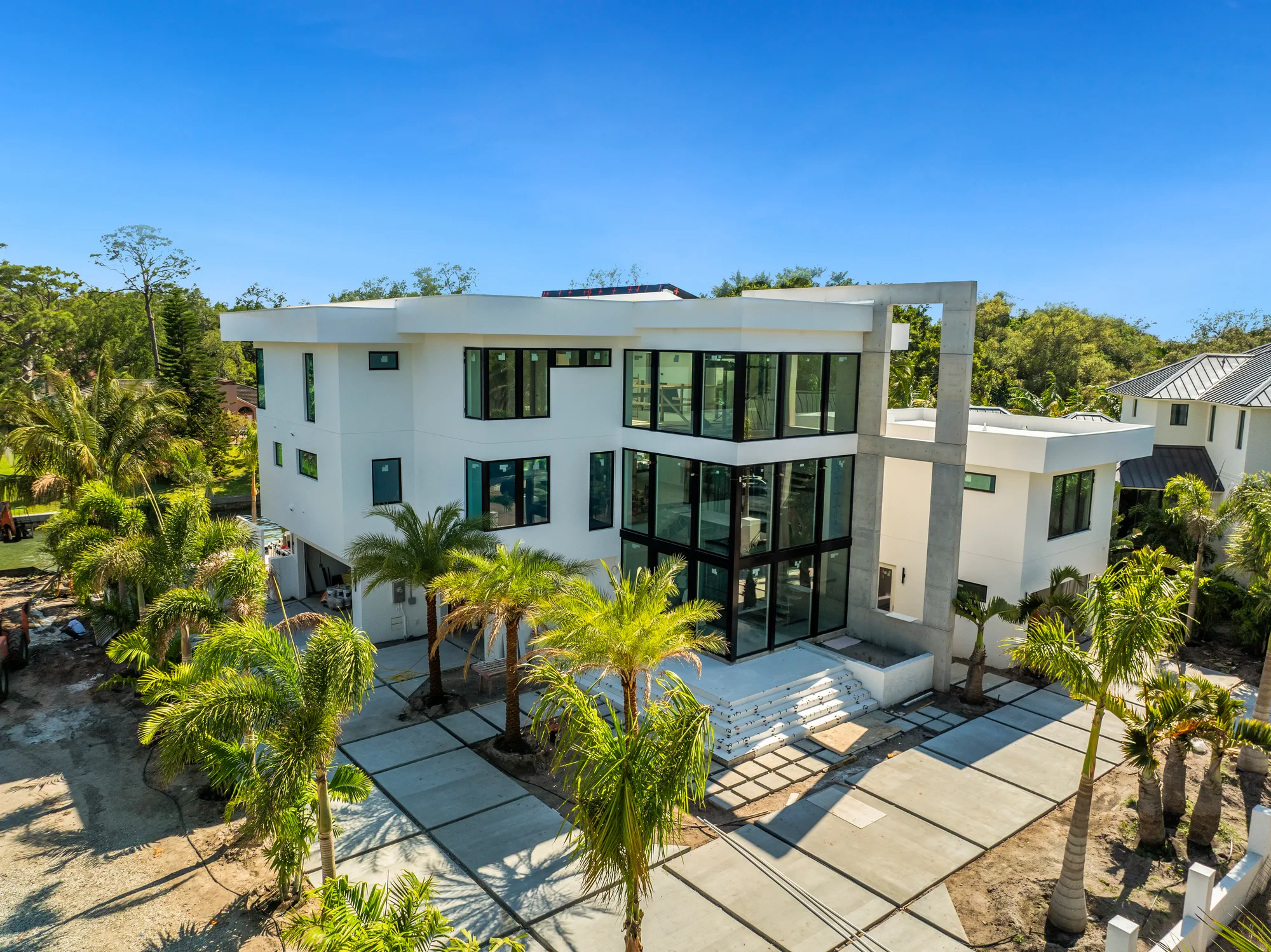 A contemporary two-storey custom home with large glass windows and a paved forecourt, framed by palms.