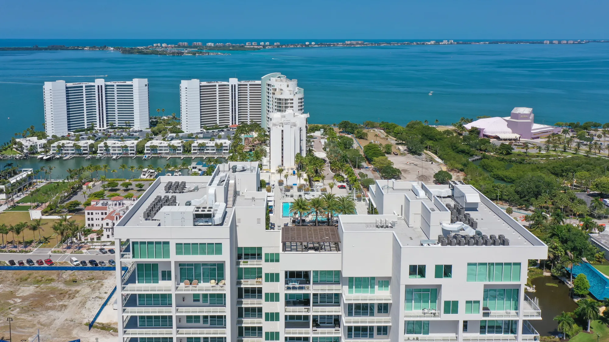 Aerial from the water of a custom bayfront estate with a pool terrace behind a rock seawall.