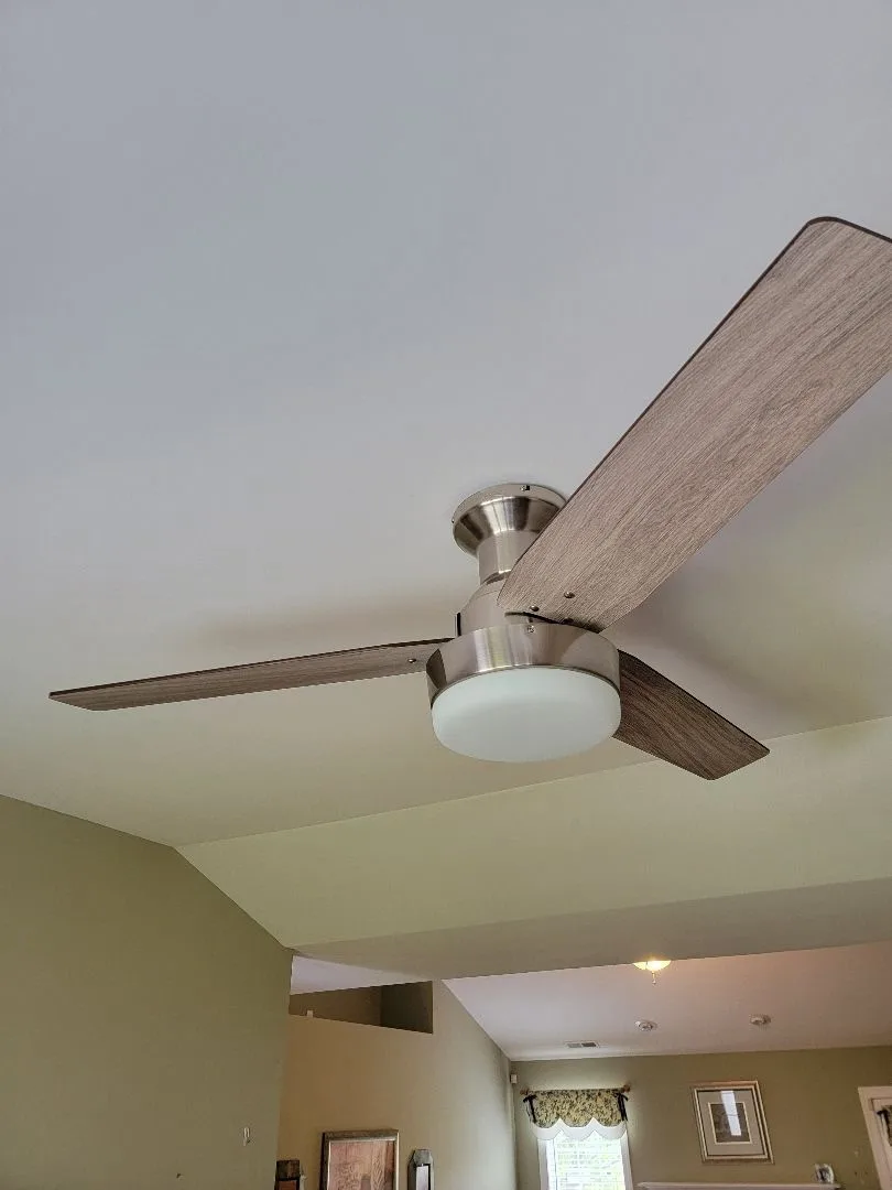 Modern ceiling fan with wooden blades and frosted light fixture installed on a white ceiling