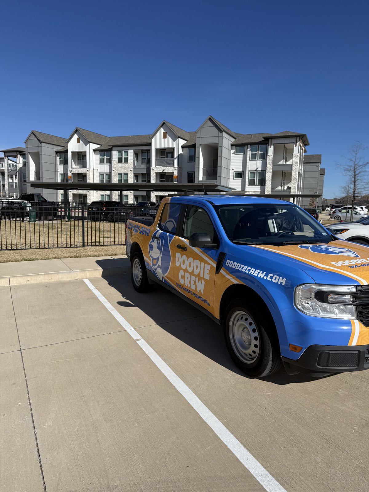 Doodie Crew blue and orange branded truck parked in front of a modern apartment building for pet waste removal service