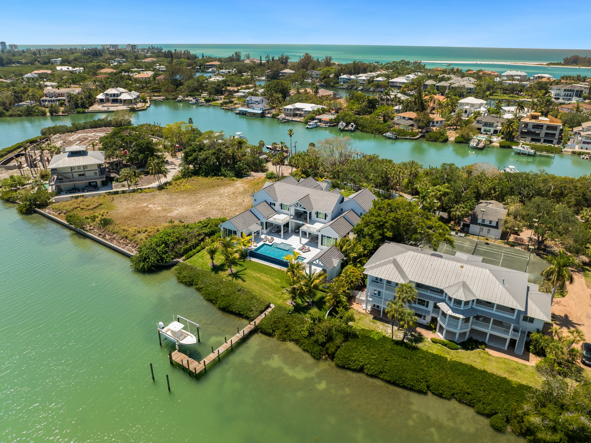 This aerial image showcases a cluster of waterfront homes surrounded by green waterways and lush landscaping. A swimming pool and dock can be seen at the foreground property, highlighting the scenic coastal living.