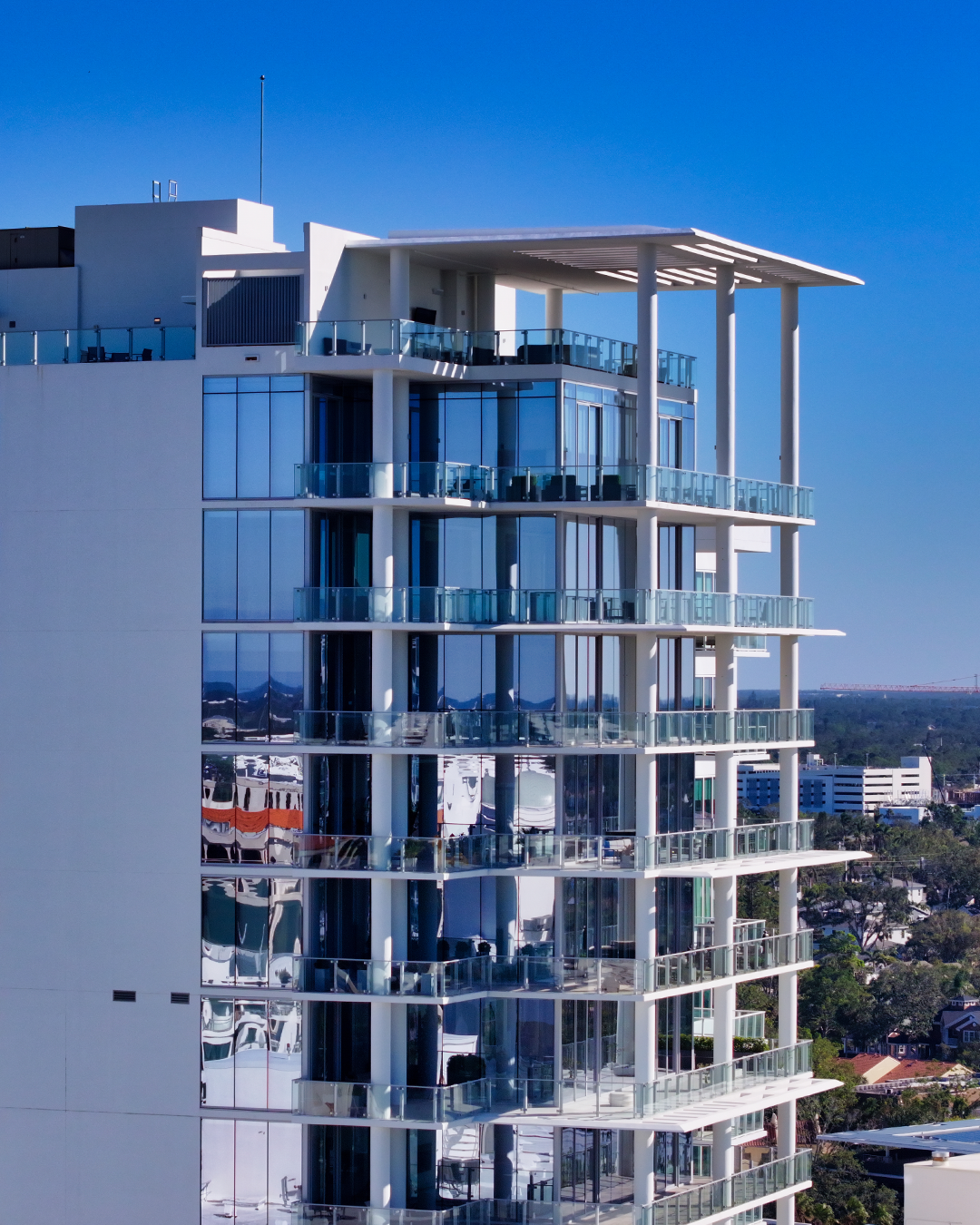 This image showcases a contemporary high-rise building featuring glass balconies and a sleek facade. The reflection on the windows highlights the surrounding urban landscape under a clear blue sky.