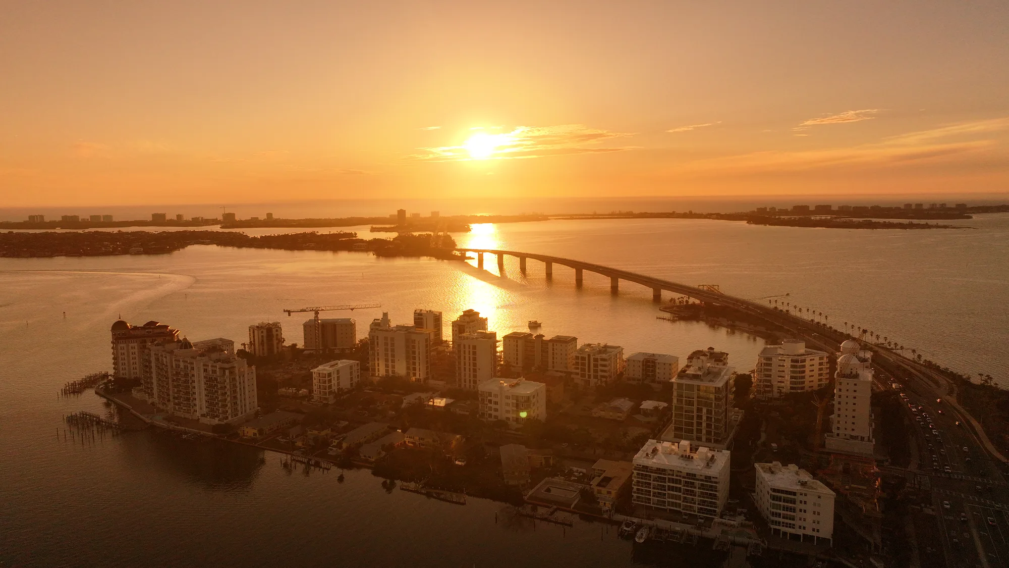 Aerial photograph at sunset looking across downtown Sarasota's waterfront towers to the Ringling Bridge and the Gulf beyond.