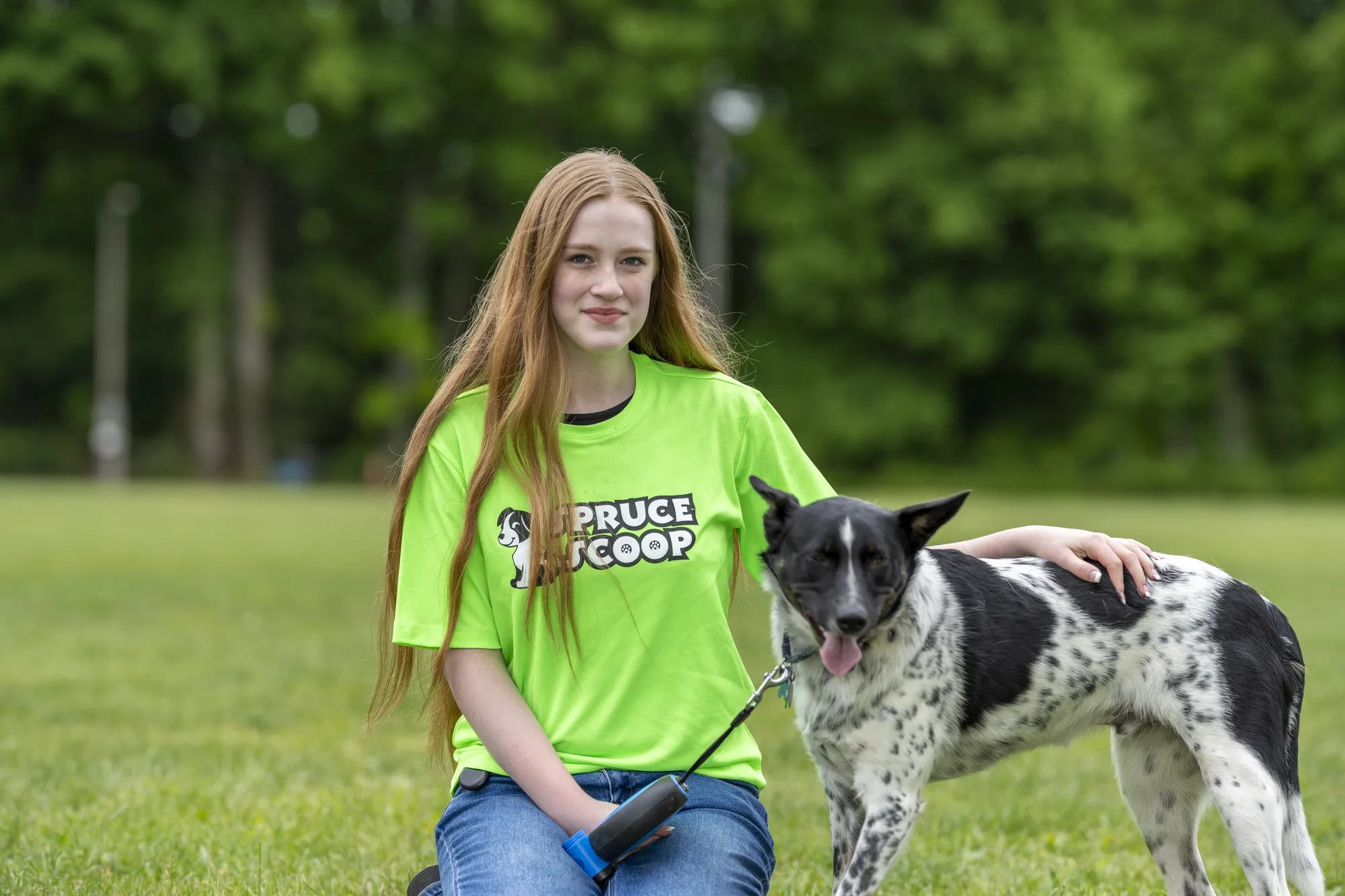A Spruce Scoop team member kneeling on the grass beside a black-and-white dog