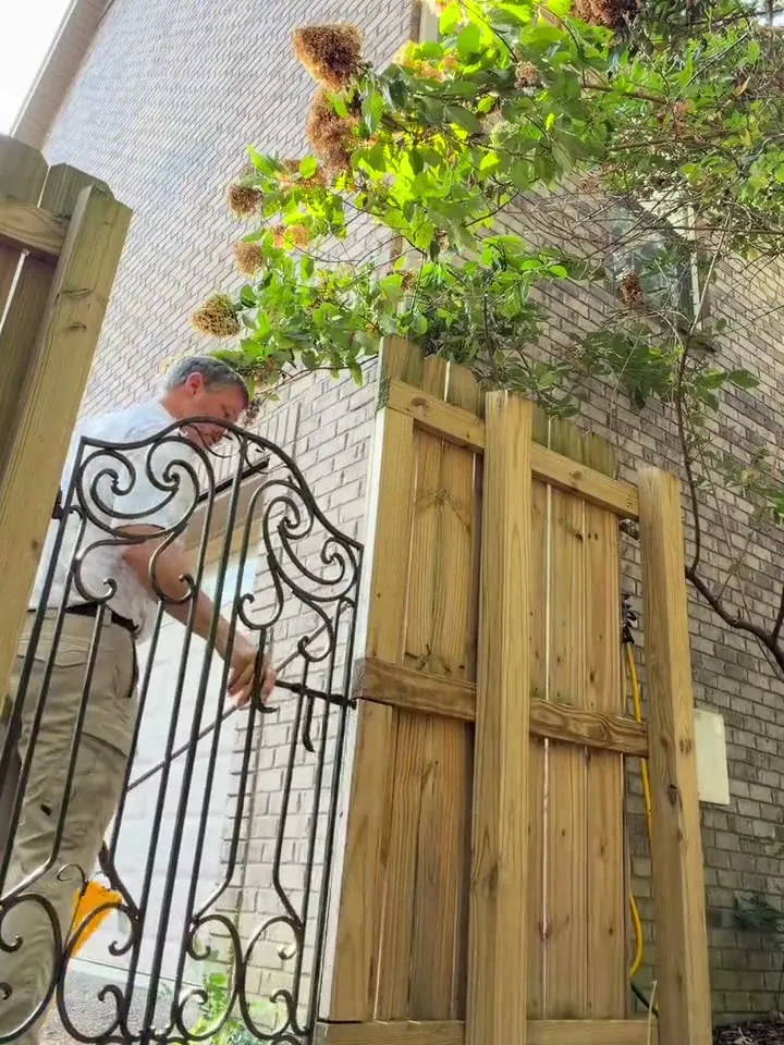 Christopher Glass latching an iron garden gate beside a wooden fence