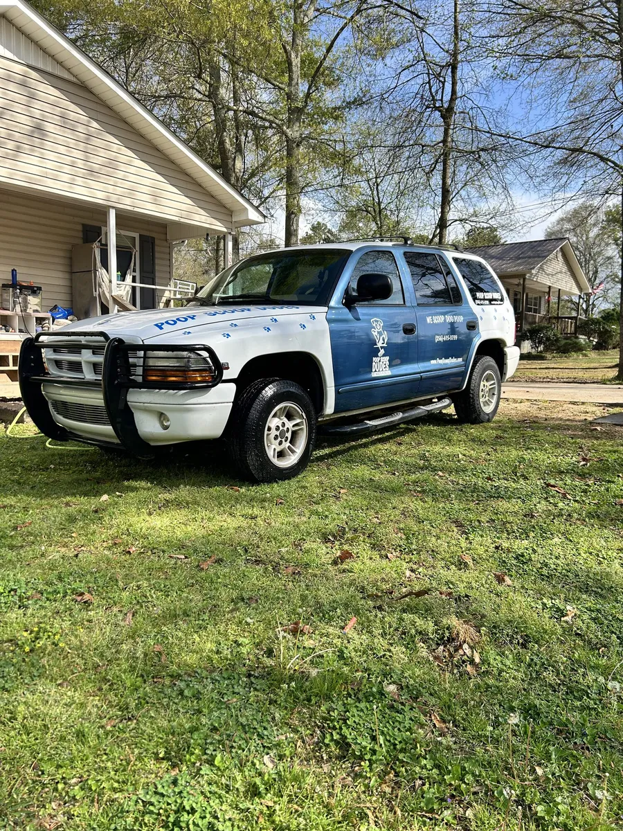 Poop Scoop Dudes branded SUV parked on a lawn in front of a home