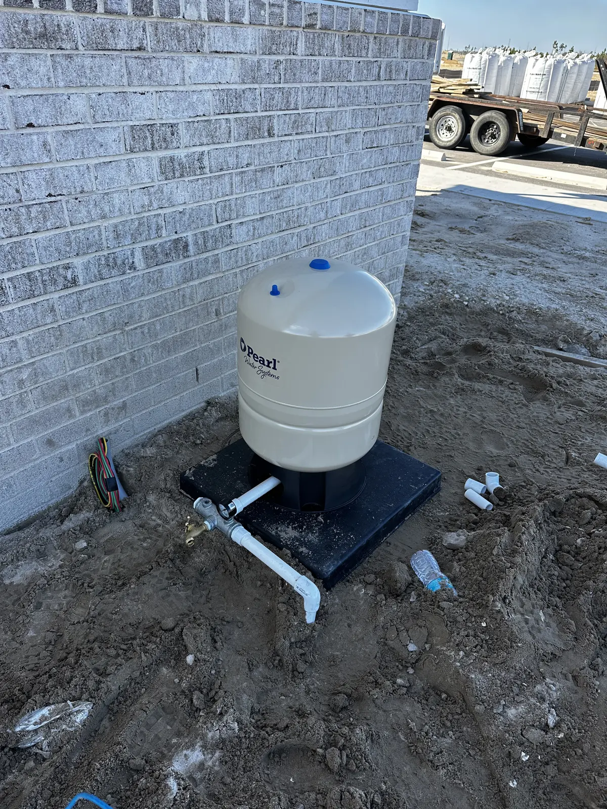 Water pressure tank with connecting pipe beside a brick wall, ground freshly dug