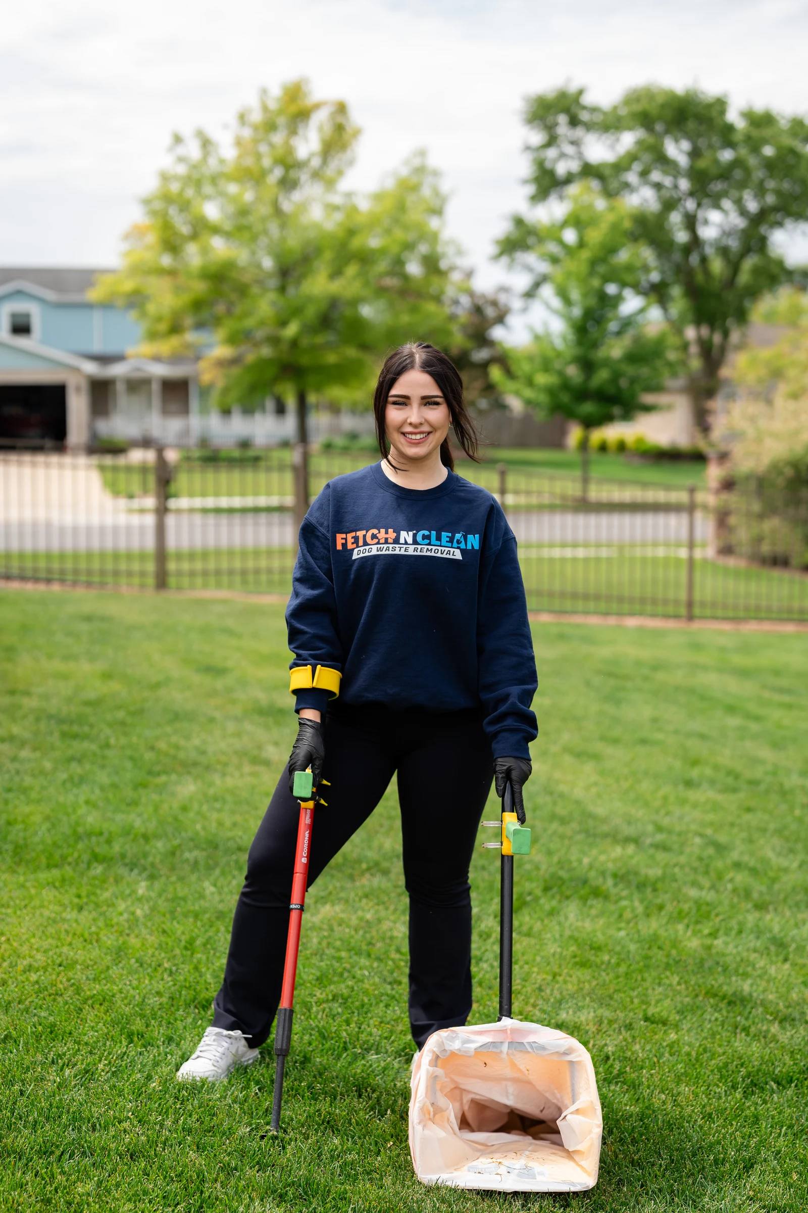 Fetch N Clean team member in gloves holding cleanup tools in a fenced backyard.