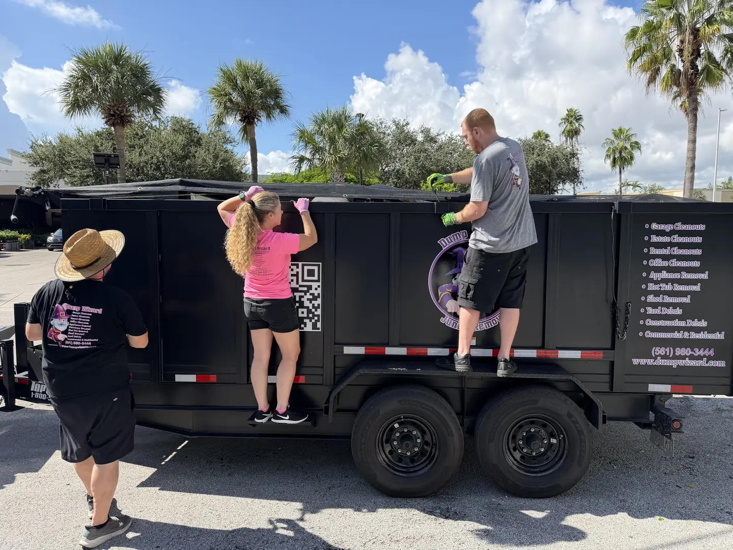 Three Dump Wizard crew members loading the wrapped trailer on a sunny Fort Lauderdale job