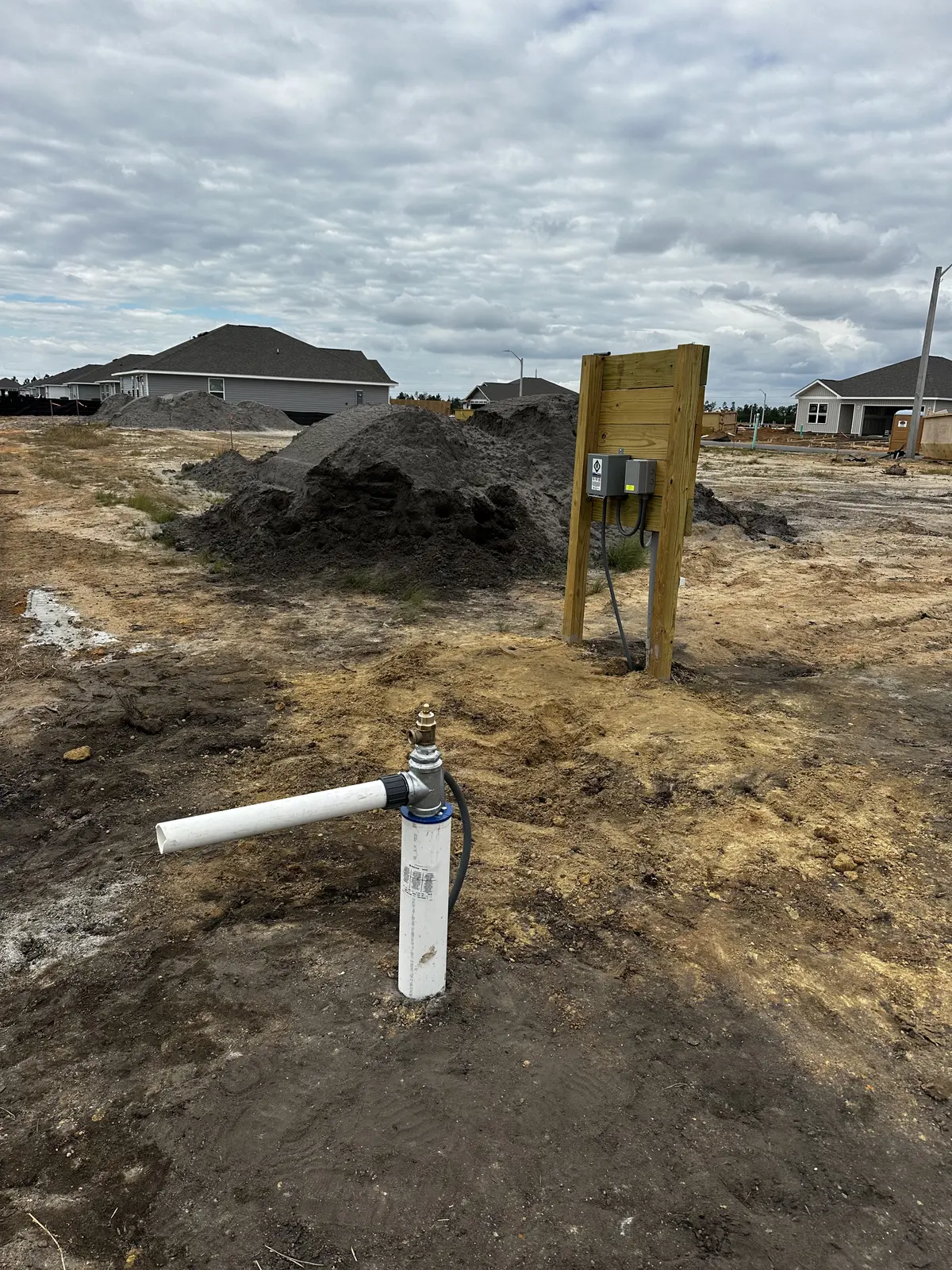 White PVC water supply connection and utility box at a construction site with partially built homes behind