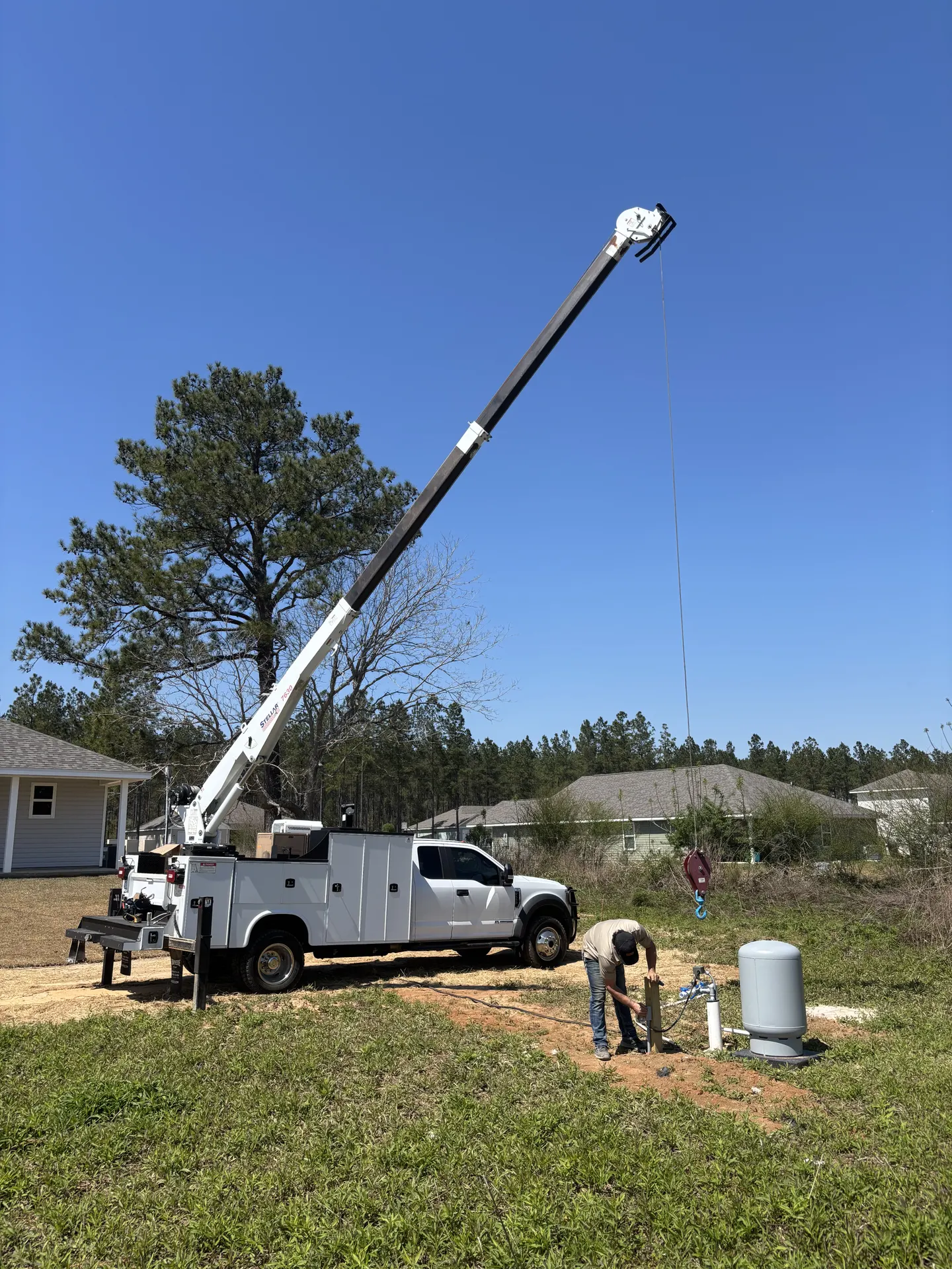 Crane truck working beside a well and pump system in a residential neighborhood