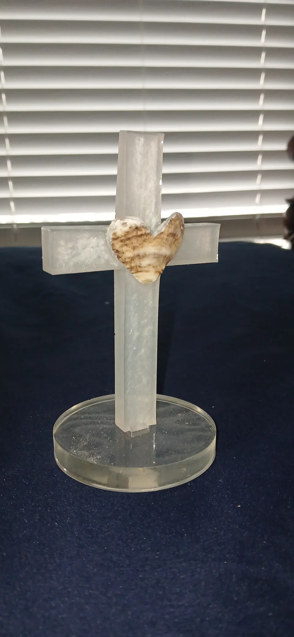 Translucent cross on a round clear base with a heart-shaped shell at its center