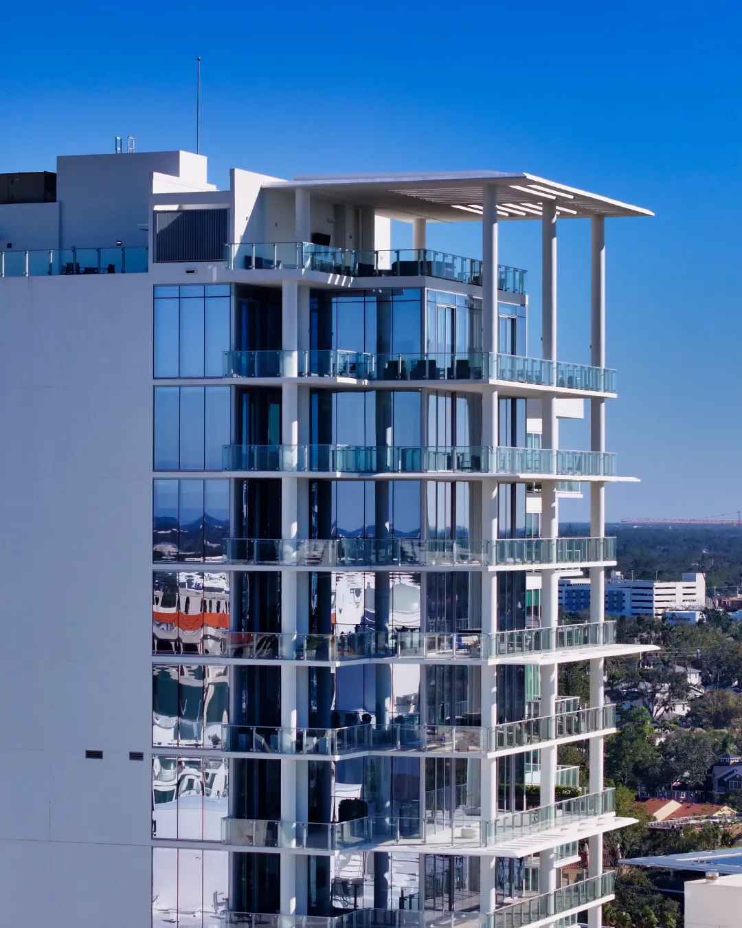 This image showcases a contemporary high-rise building featuring glass balconies and a sleek facade. The reflection on the windows highlights the surrounding urban landscape under a clear blue sky.
