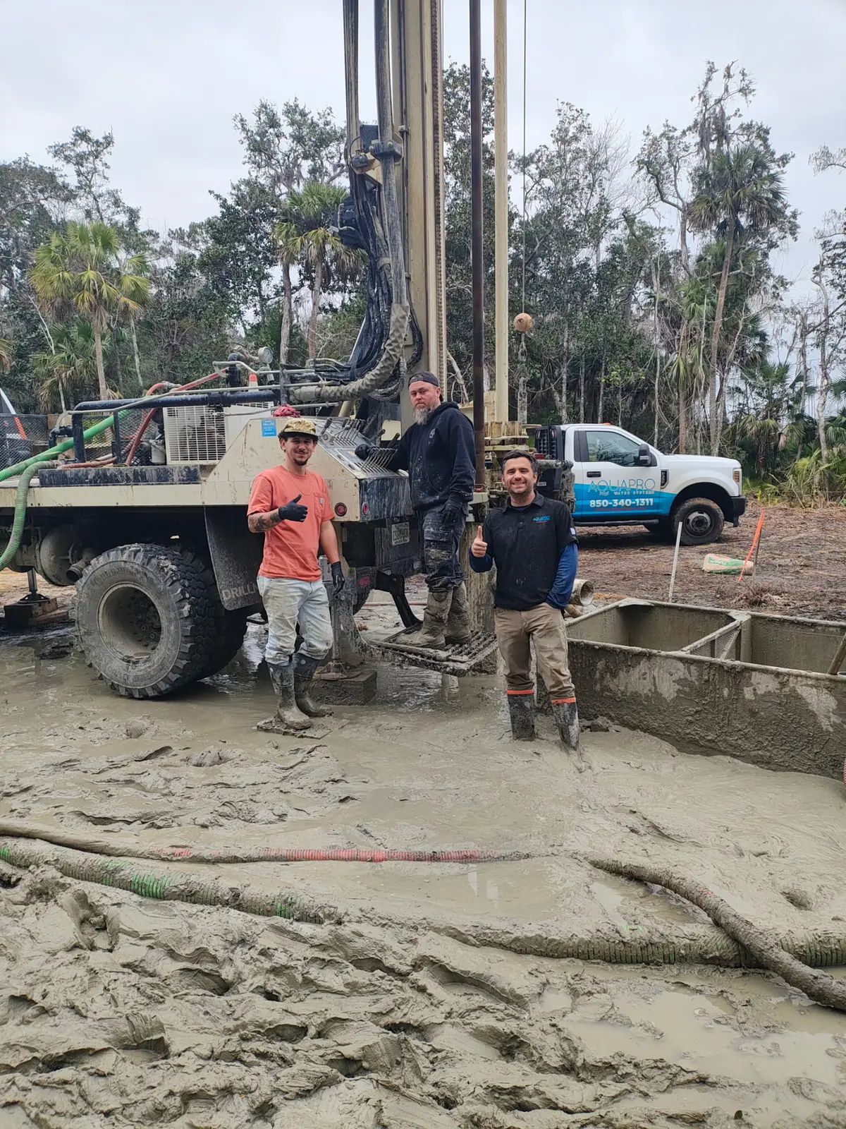 Three crew members standing beside the drilling rig, palms in the distance