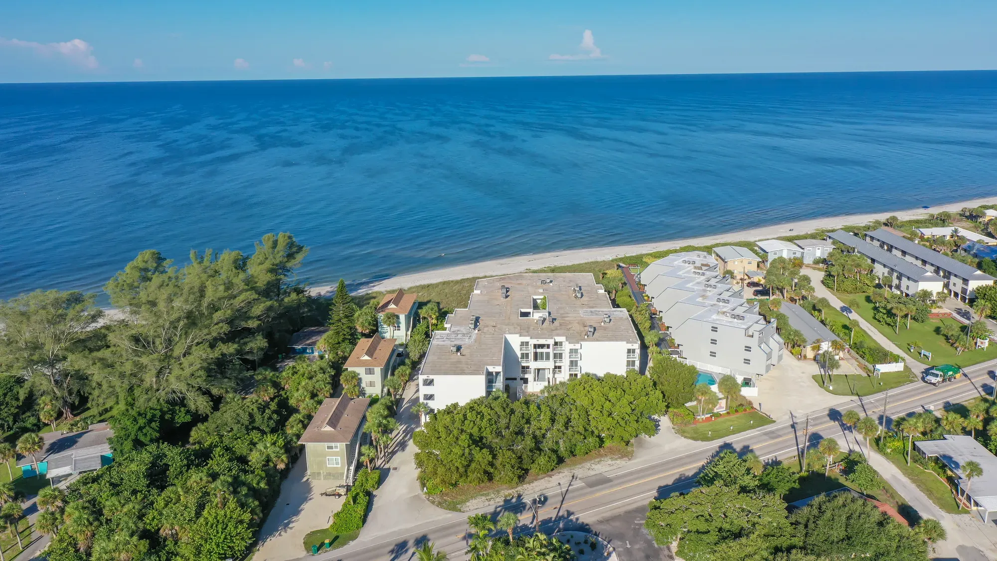 Aerial of The Collection Residences in Sarasota, a white multi-storey residential building among the downtown low-rise blocks, with the Gulf beyond.