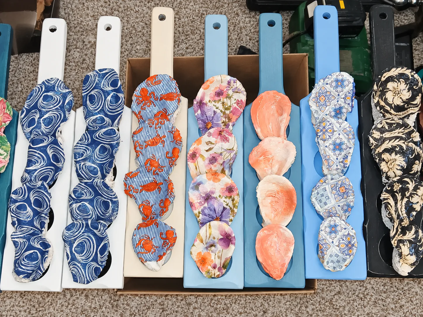 Row of painted wooden paddles lined with oyster shells in floral, wave, crab and tile patterns