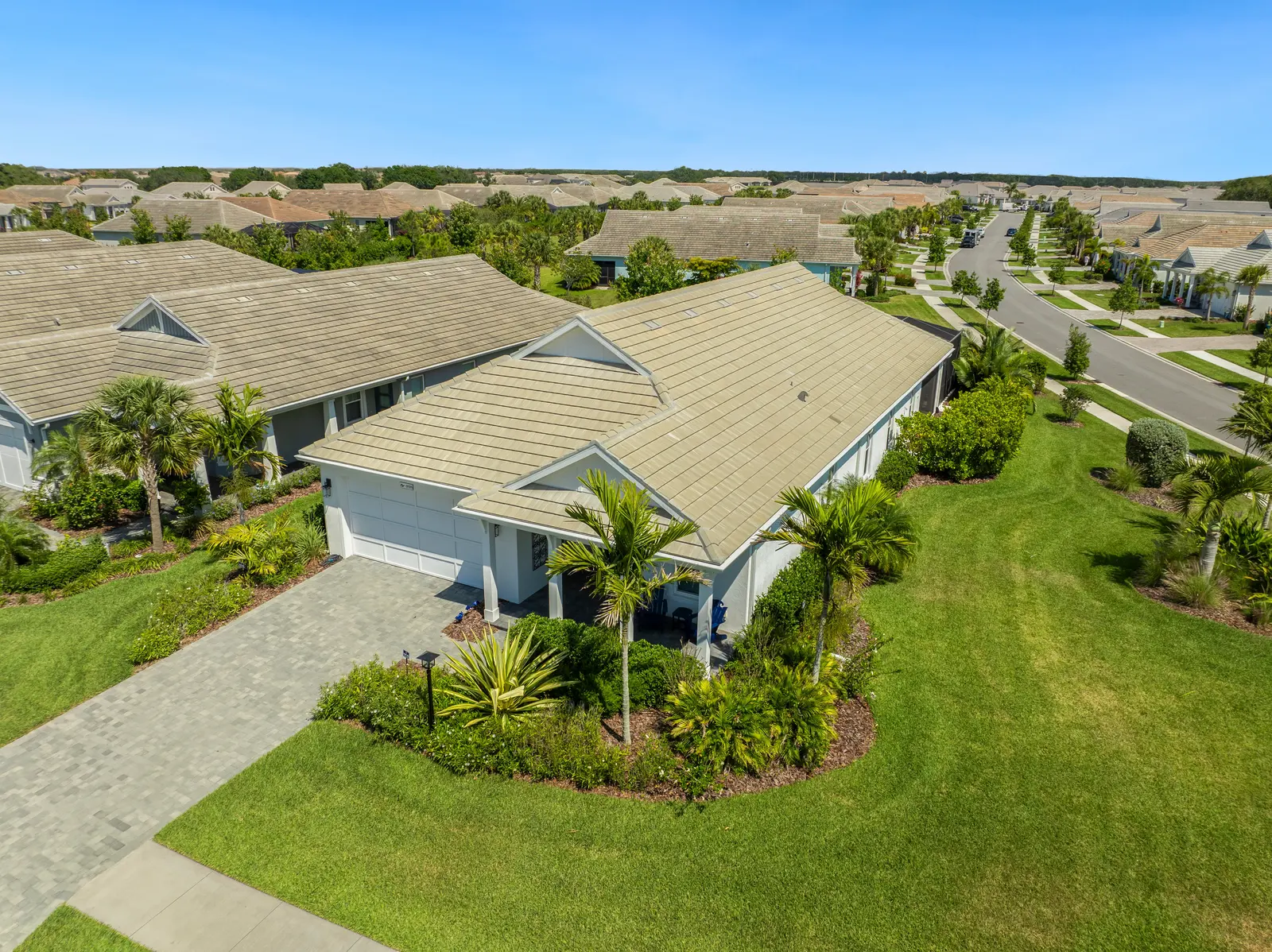 This aerial view showcases a modern single-story home surrounded by well-manicured landscaping and palm trees. The neighborhood features a series of similar houses and well-maintained streets, emphasizing a suburban living environment.