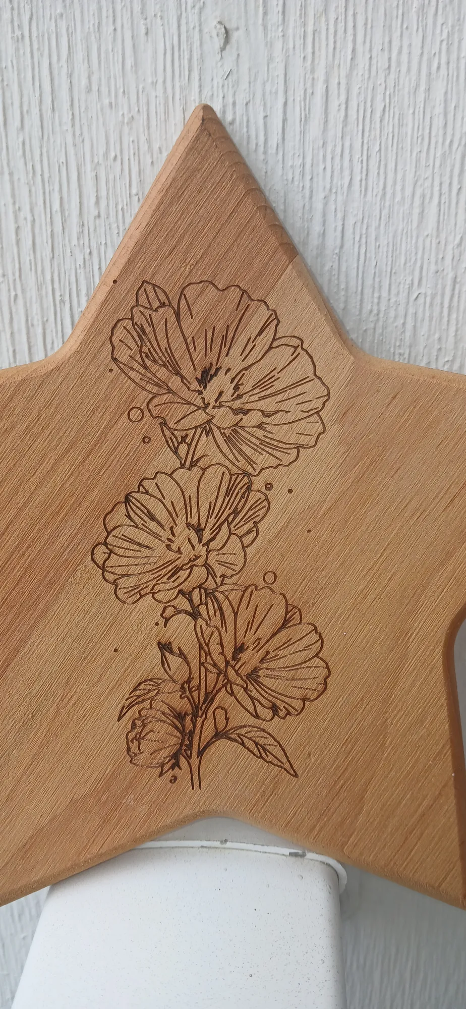 Wooden star engraved with a stem of three line-drawn flowers, against a white textured wall