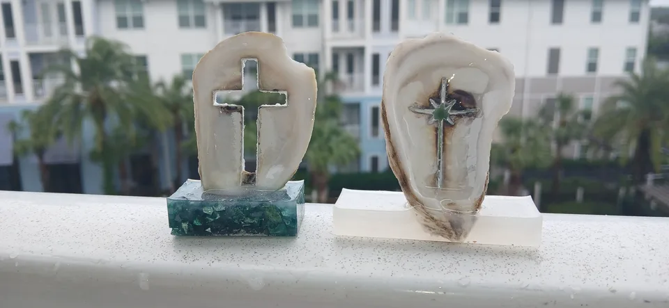 Two upright oyster shells with cross-shaped cutouts on green and white bases on a balcony rail